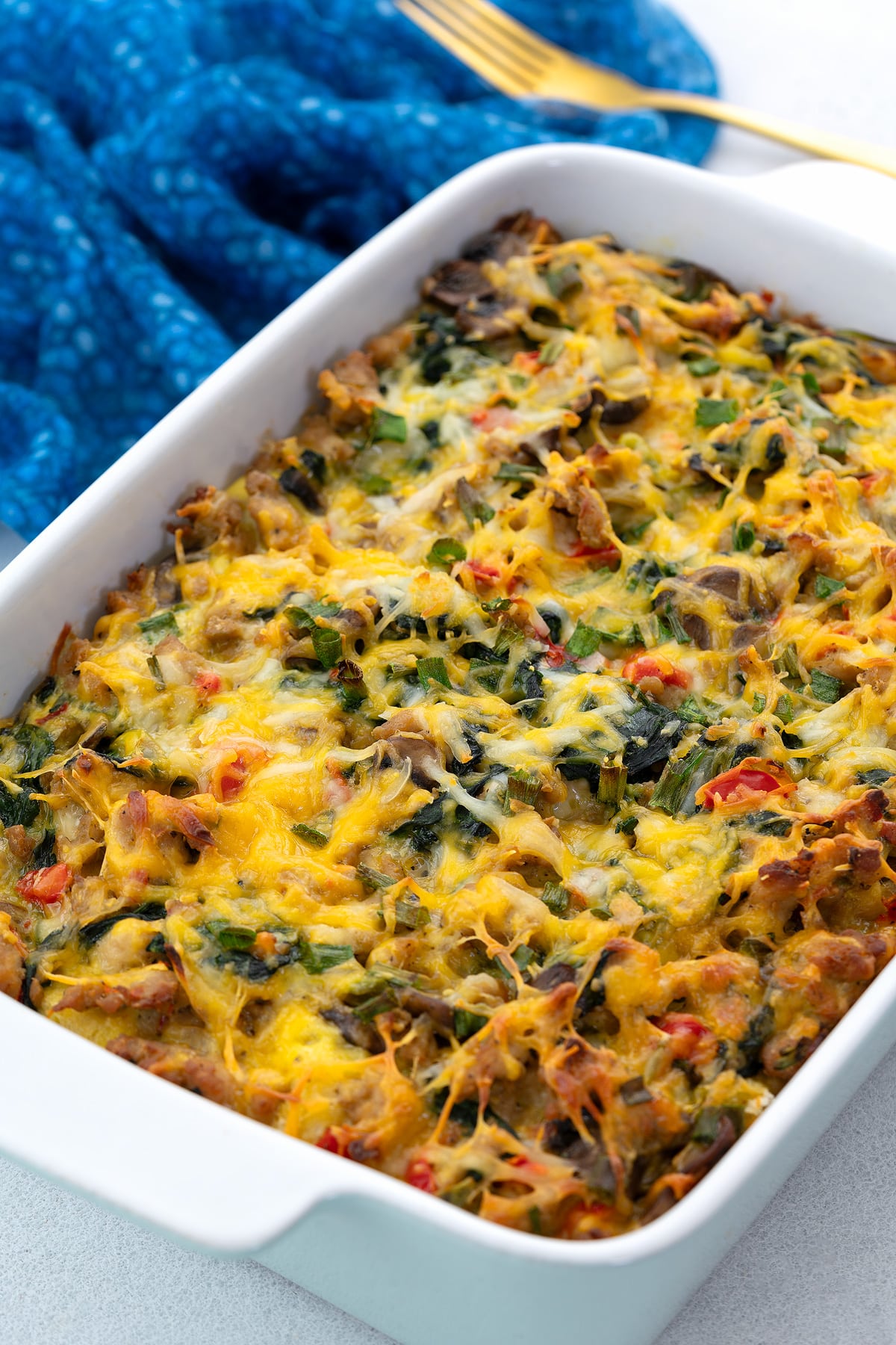 Homemade breakfast casserole in a white baking dish on a white table top with a blue towel and a golden fork.