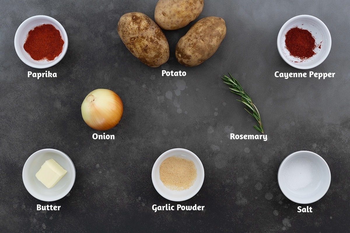 A list of ingredients for breakfast potatoes, including paprika, potato, cayenne pepper, onion, rosemary, butter, garlic powder, and salt, displayed on a grey table top.