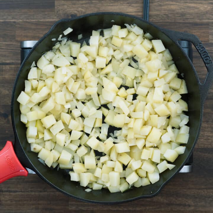 An iron skillet with potatoes and onion.