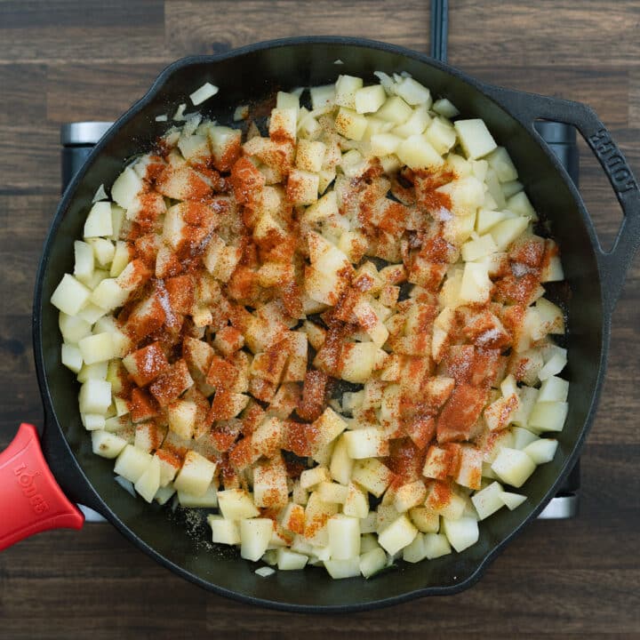 An iron skillet with potatoes seasoned with spice powders.