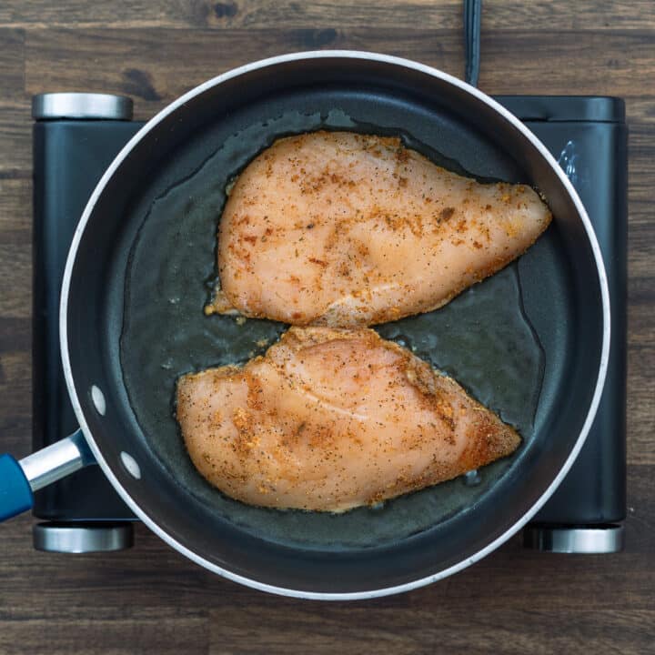 Chicken breast frying in a pan.