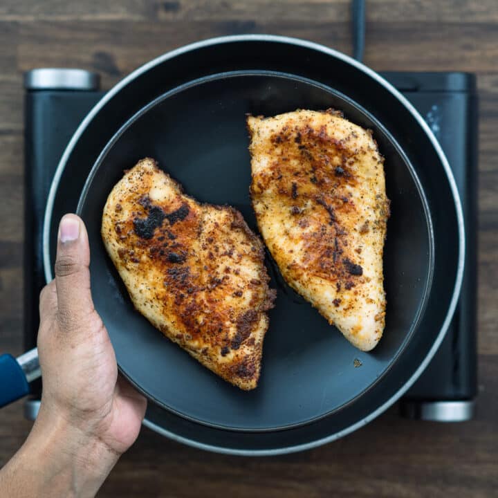 Pan seared chicken breast on a black plate.