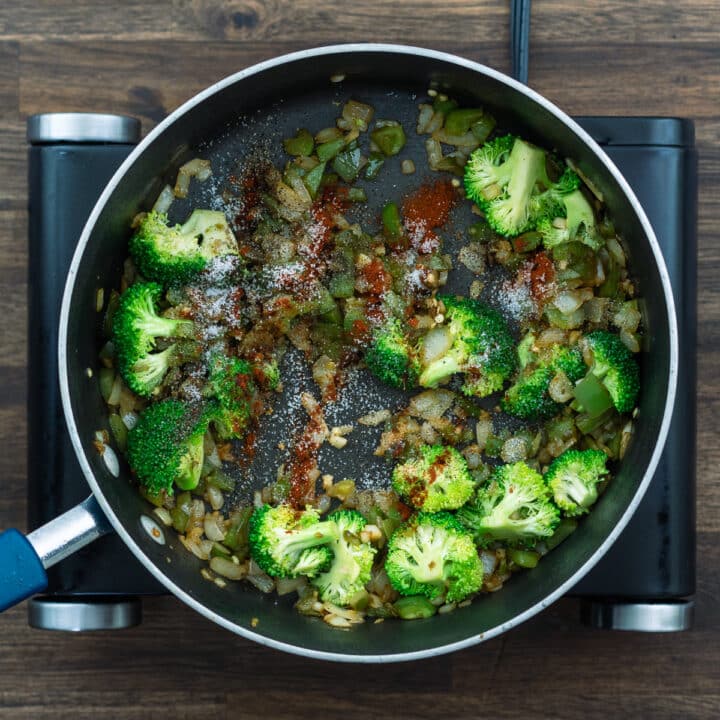 A pan with broccoli and aromatics seasoned with seasoning powders.