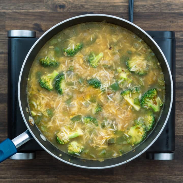 A pan with veggies, rice that are boiling in a chicken broth.