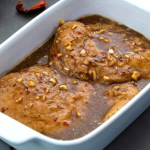 Chicken marinade in a white dish, mixed with chicken breasts, placed on a grey table.