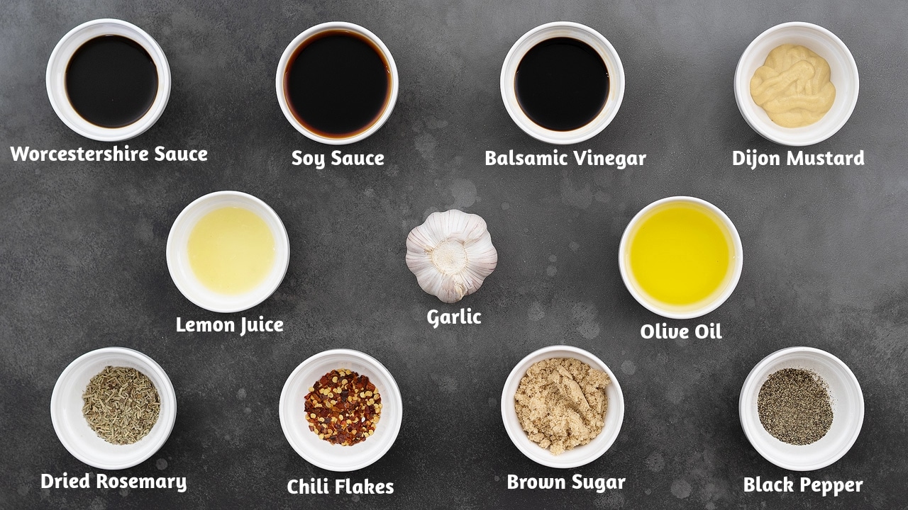 Chicken marinade ingredients arranged on a grey table, including: Worcestershire sauce, soy sauce, balsamic vinegar, Dijon mustard, lemon juice, garlic, olive oil, dried rosemary, chili flakes, brown sugar, and black pepper.