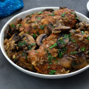 A homemade chicken marsala dish served in a white bowl on a grey table.