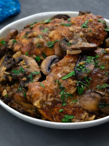 A homemade chicken marsala dish served in a white bowl on a grey table.