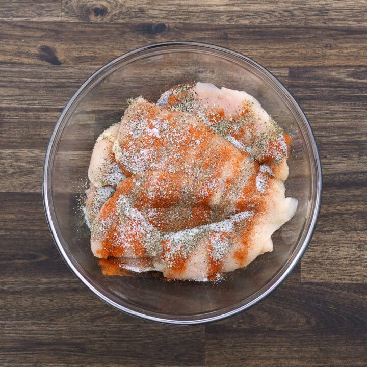 A bowl with chicken breast seasoned with basic seasonings.
