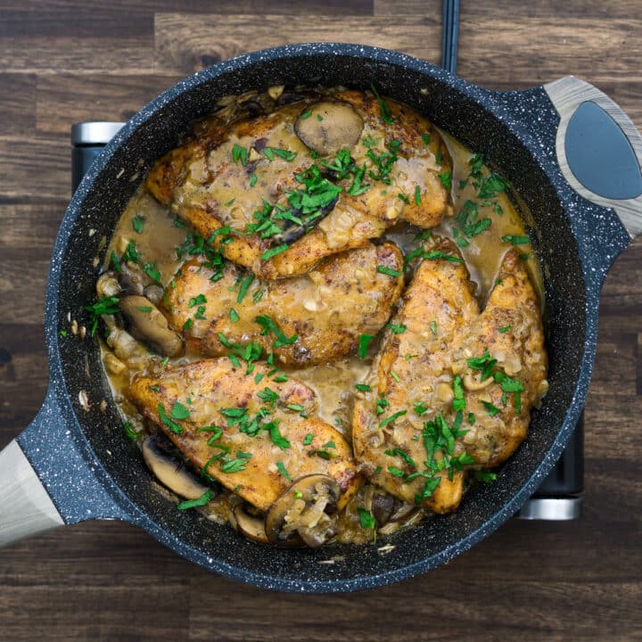 A pan with Chicken Marsala garnished with parsley leaves.