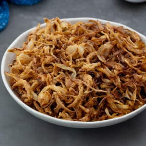 Classic and French fried onions in a white bowl placed on a gray table.