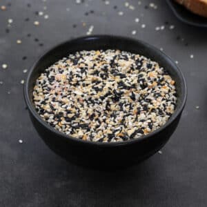Everything bagel seasoning mix on a black plate placed on a grey table.