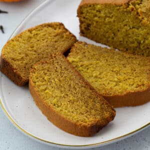 Three slices of pumpkin bread on an oval white plate on a white table.