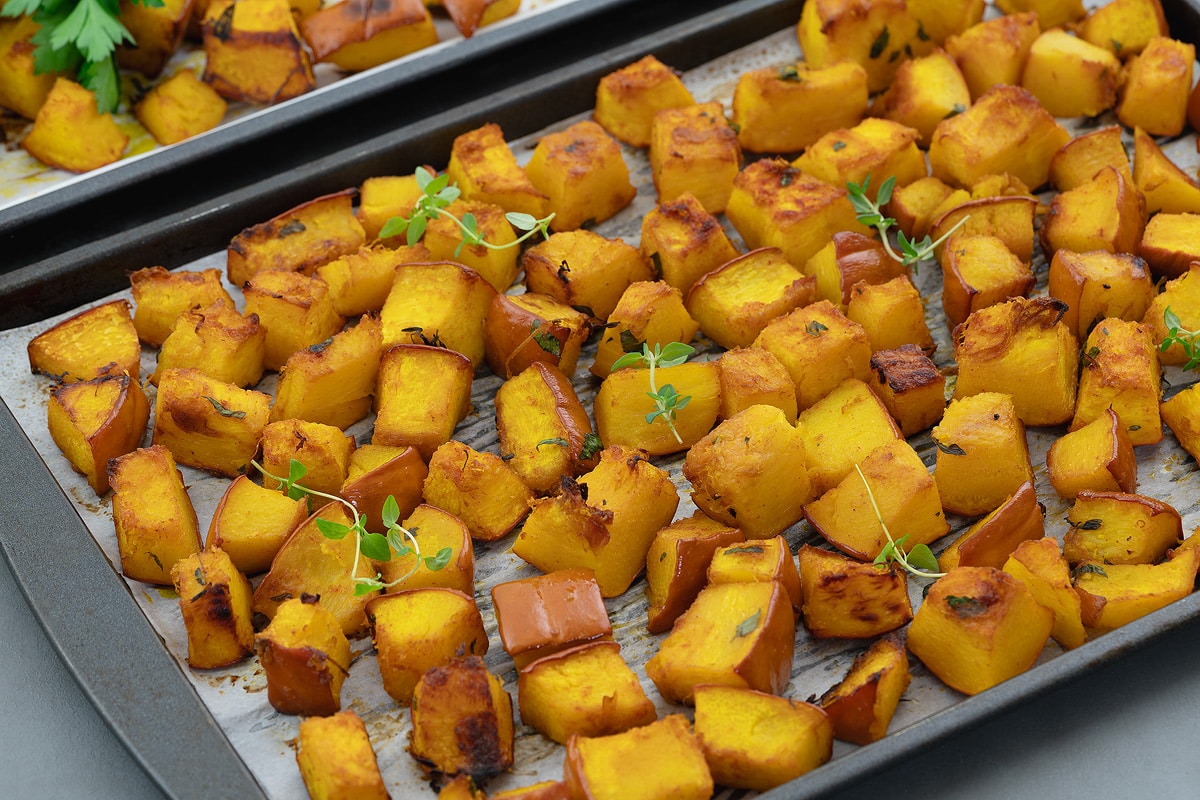 Roasted pumpkin in a baking tray. Sliced lemon and a golden fork placed around.