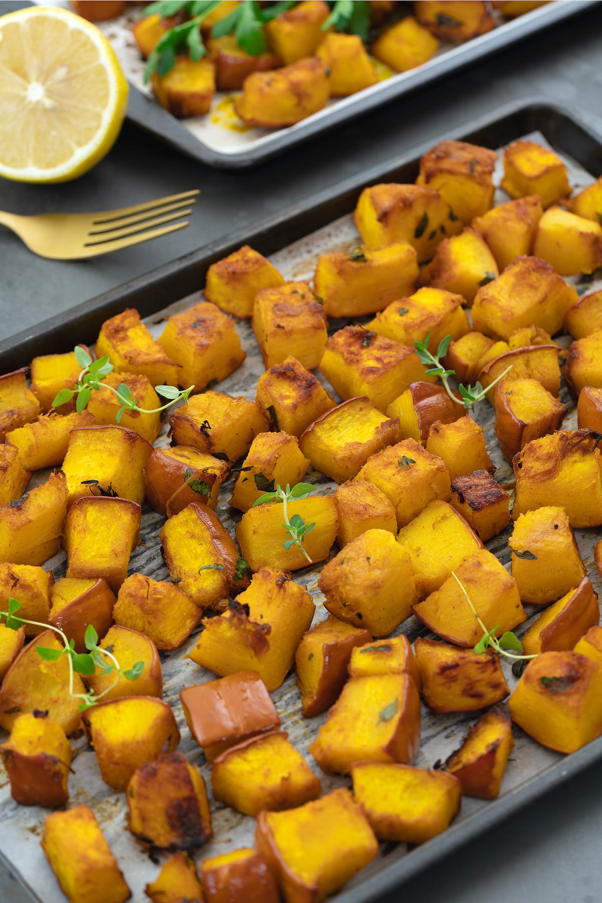 Roasted pumpkin in a baking tray. Sliced lemon and a golden fork placed around.