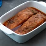 White baking tray filled with salmon fillets marinated in a freshly prepared homemade salmon marinade.