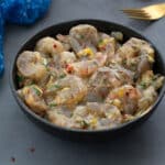 Marinated shrimp in a black bowl on a gray table, surrounded by a blue towel, a golden fork.