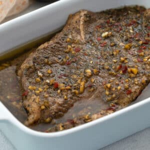 Steak marinade with steak cuts in a white dish on a white table.