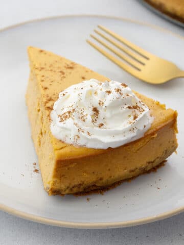 Pumpkin cheesecake served on a white plate with a gold fork, set on a white table.