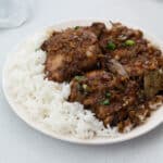 Filipino chicken adobo served on a white plate with a side of rice and placed on a white table.