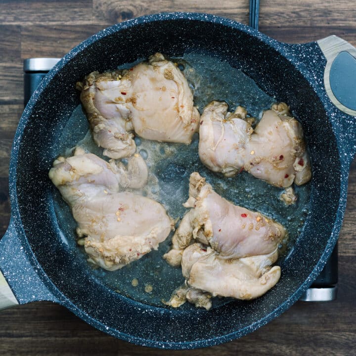 A pan with marinated chicken thighs frying in oil.