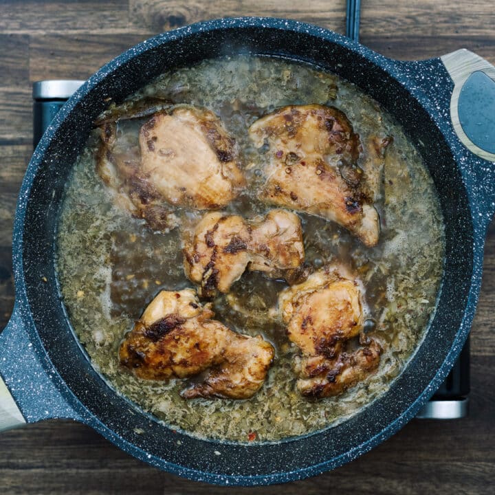 A pan with fried chicken thighs simmering in adobo sauce.