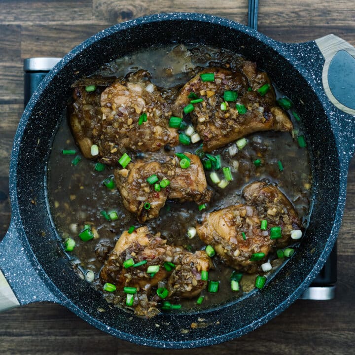 A pan with Filipino Chicken Adobo garnished with spring onions.