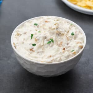 Homemade French onion dip served in a white bowl on a gray table.