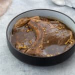 Pork chop marinade in a brown bowl, placed on a white table.