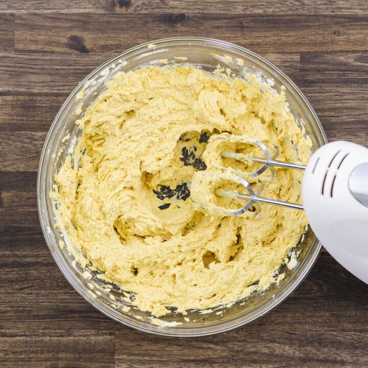 A bowl displaying a blend of butter mixture combined with pumpkin puree, using a beater.