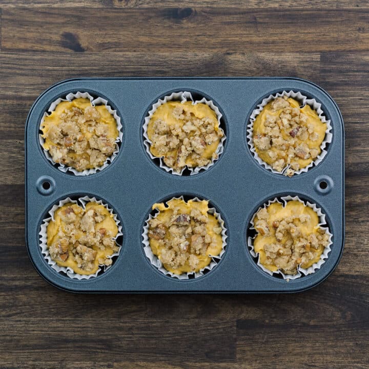 A muffin tray with pumpkin muffin batter topped with streusel toppings.