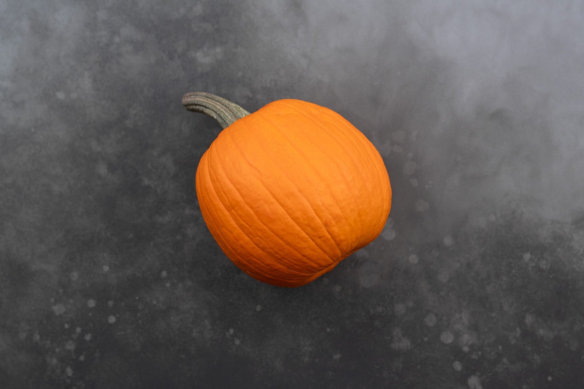 A whole pumpkin placed on a grey table.