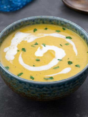 Homemade pumpkin soup served in a green patterned bowl on a gray table. A wooden spoon, and a blue towel are neatly arranged around the bowl.