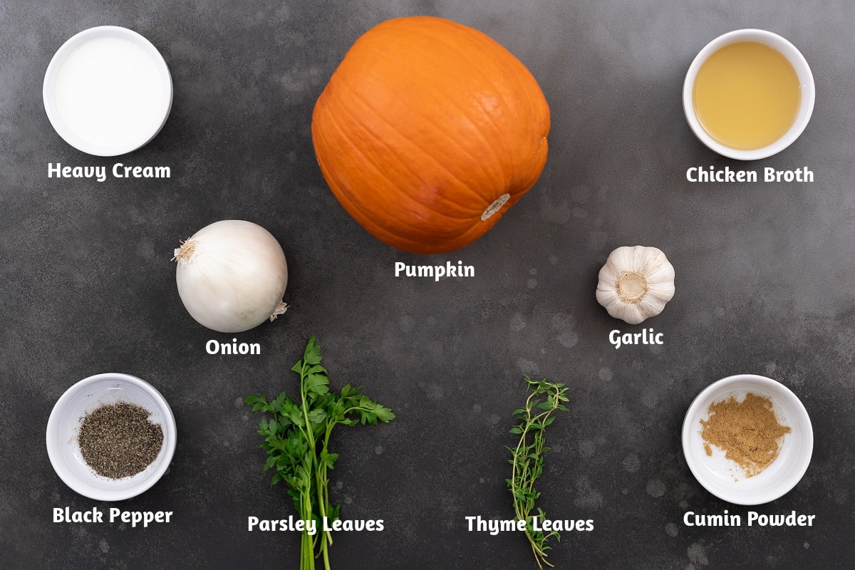 Pumpkin soup ingredients on a table, including heavy cream, pumpkin, chicken broth, onion, garlic, black pepper, parsley, thyme, and cumin powder.