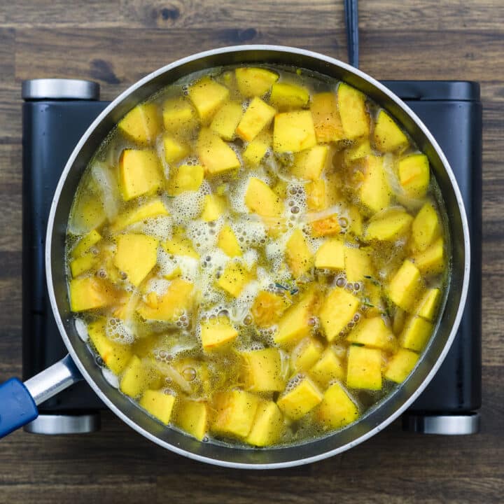 A pan with pumpkin cooking in a chicken broth.