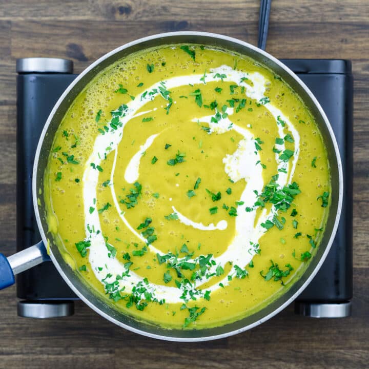 A pan with pumpkin soup garnished with heavy cream and parsley leaves.