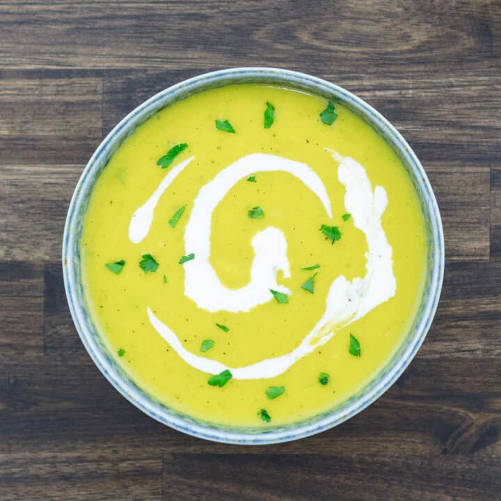 Pumpkin Soup served in a bowl garnished with heavy cream and parsley leaves.
