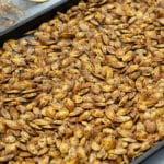 Roasted pumpkin seeds on a baking tray, placed on a white table.