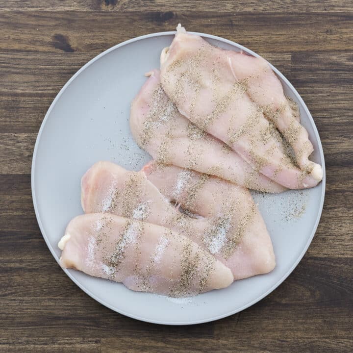 Plate of seasoned chicken breasts with black pepper and salt.