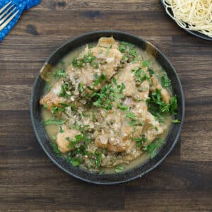 Chicken Piccata served with sauce, garnished with parsley and lemon slices in a bowl.