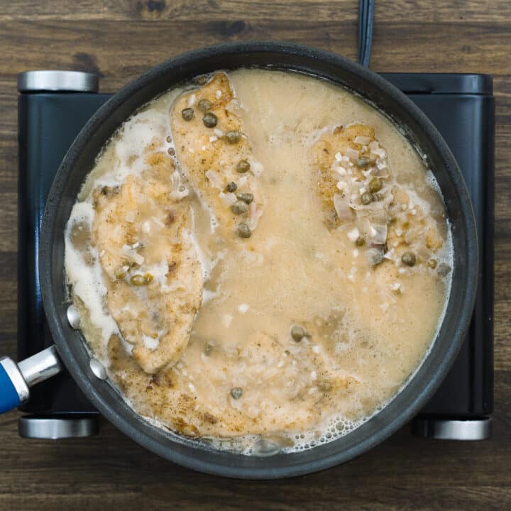 Pan with chicken breast cooking in lemon butter sauce.