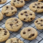 Chewy chocolate chip cookies on a black baking rack, placed on a white table.
