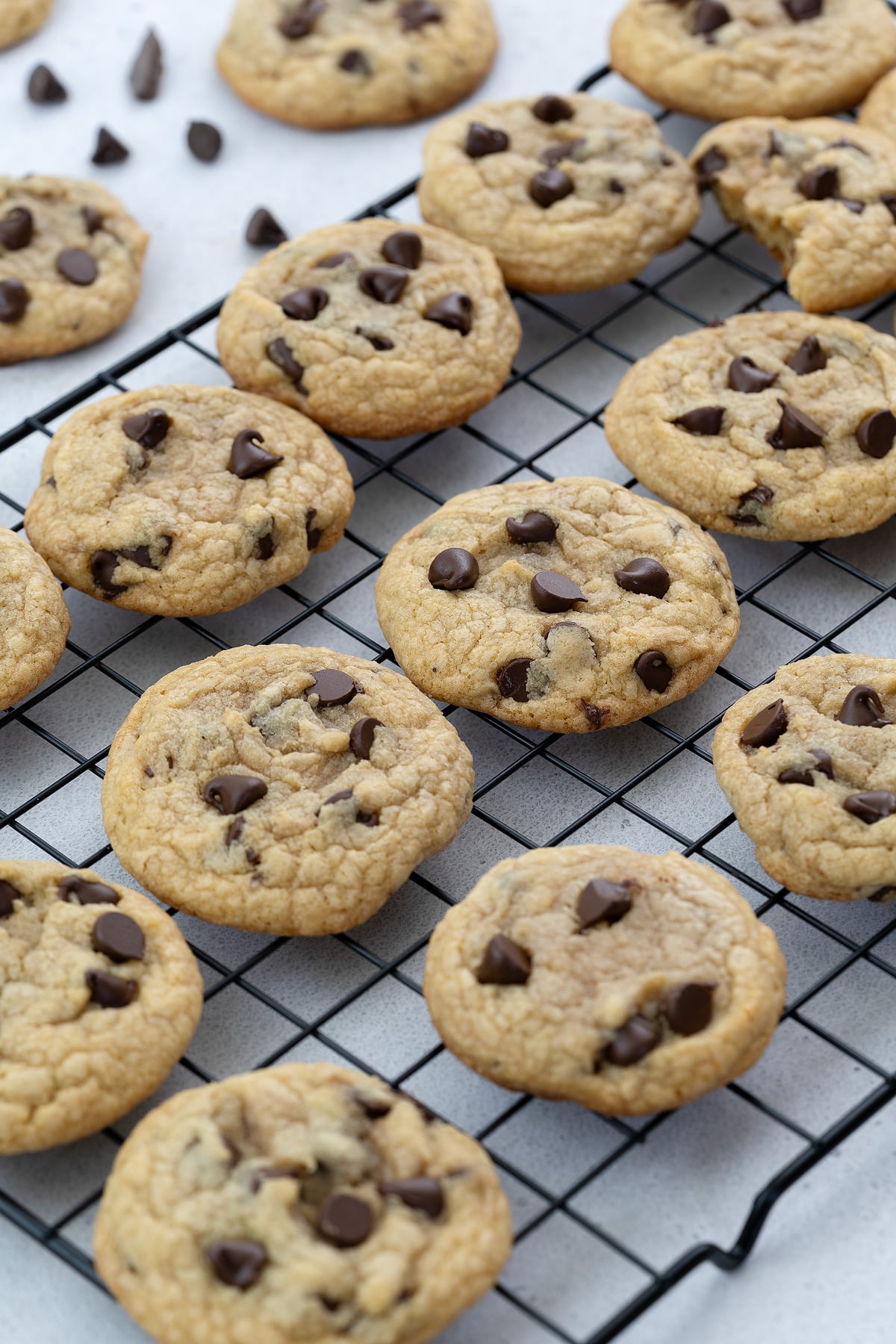 Chewy chocolate chip cookies on a black baking rack, placed on a white table.
