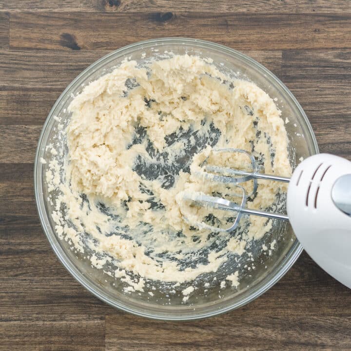 A bowl with butter and sugar mixed using an electric beater.