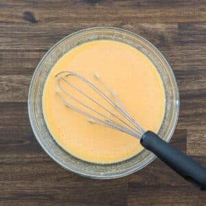 A bowl filled with a mixture of pumpkin puree and milk, with a whisk.