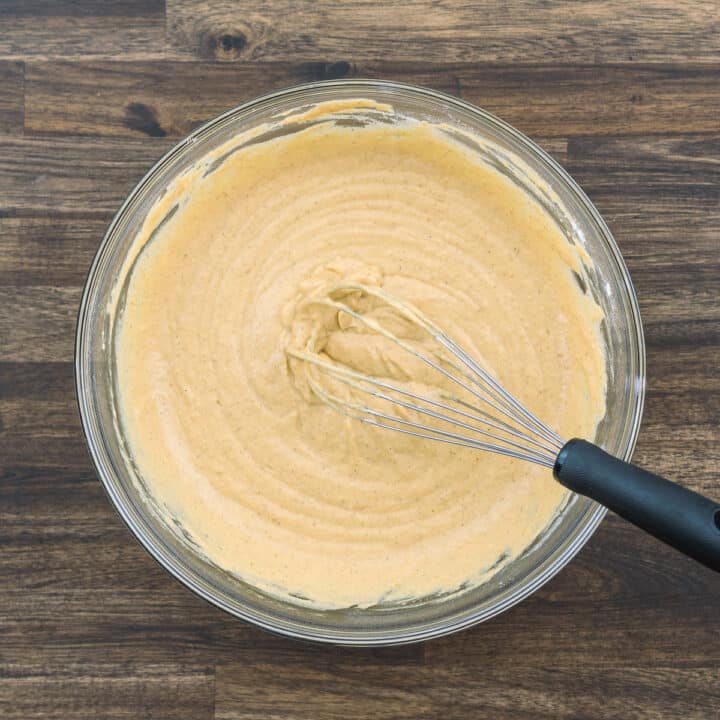 A bowl filled with pumpkin pancake batter along with a whisk.