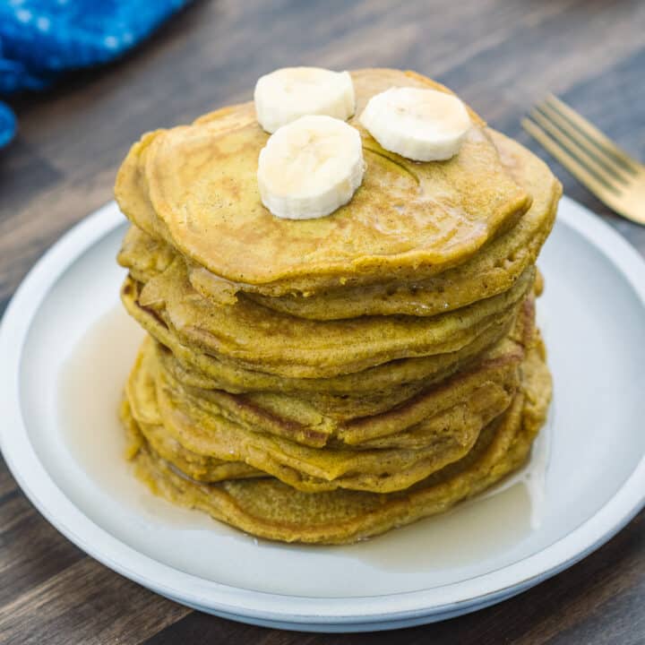 A plate with stacked pumpkin pancakes served with maple syrup and banana slices.