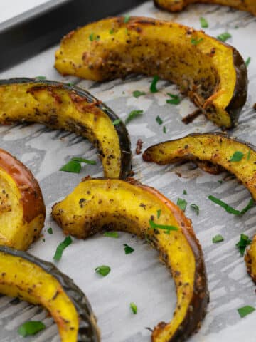 Slices of roasted acorn squash in a baking tray on a white table.
