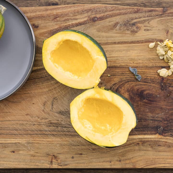 Halved acorn squash on a cutting board, seeds neatly removed alongside.