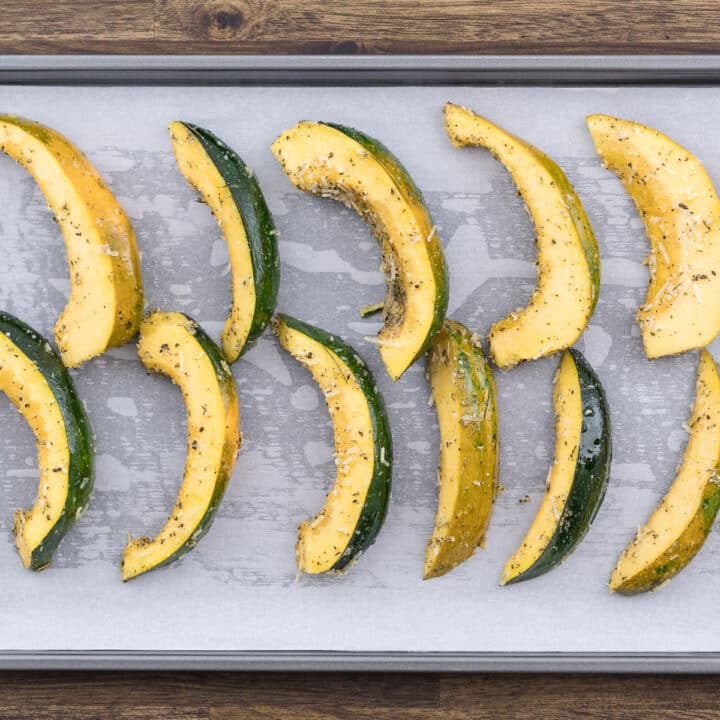 Arrangement of seasoned acorn squash slices placed on a parchment-lined baking tray.